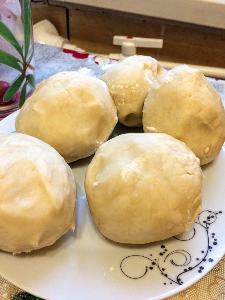5 balls of dough placed on a plate, ready to be flattened for dessert. The plate is white, but with a swirl design on a small part of it.